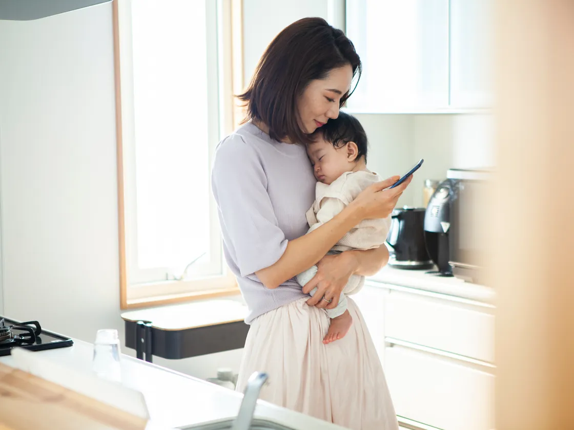 子どもを抱きながらスマホで連絡を確認する保護者