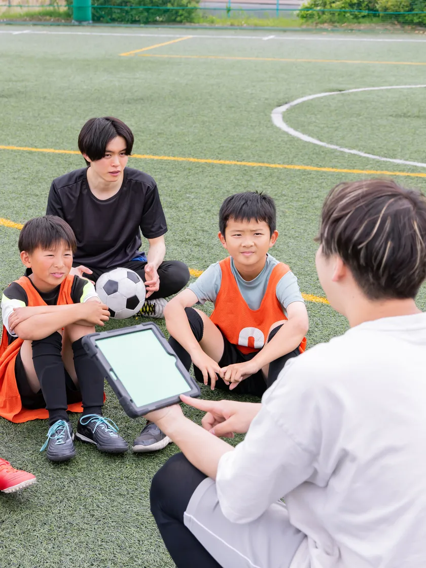 タブレットを見せながら子どもたちに話すコーチ
